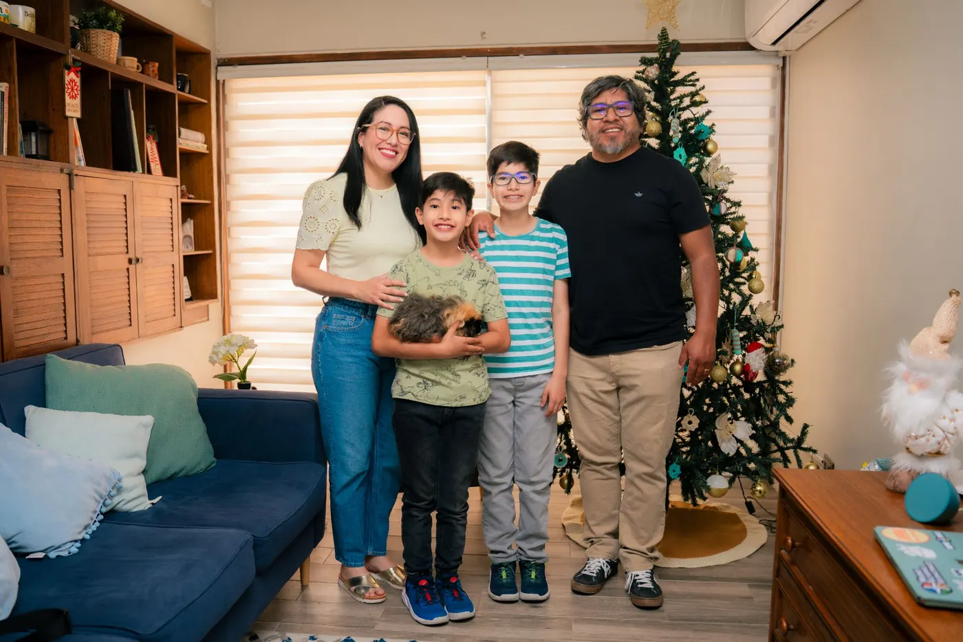 La familia completa de pie en la sala, abrazados, con el cuy en brazos de Mateo.