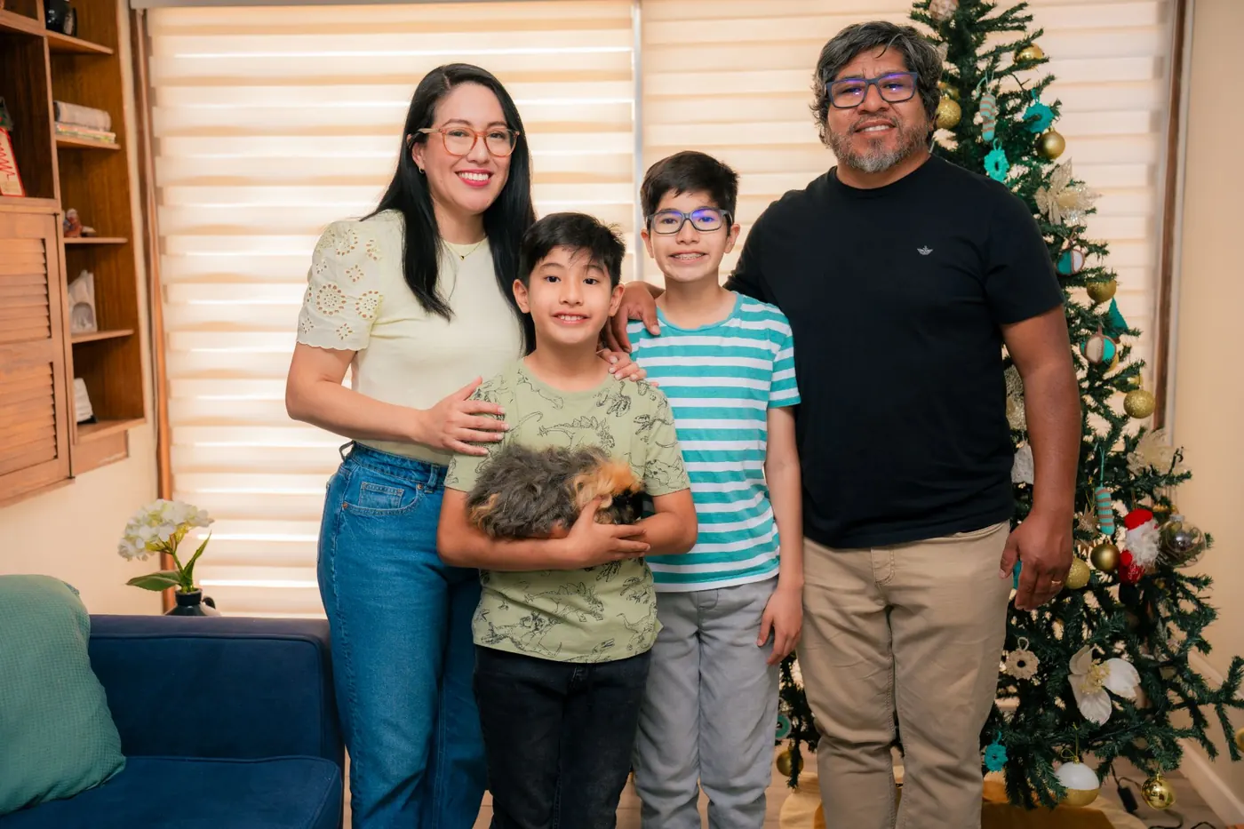 David, Ruth, Lucas y Mateo Huanca Bravo de pie en su sala, junto al árbol de Navidad; Mateo sostiene a su cuy.