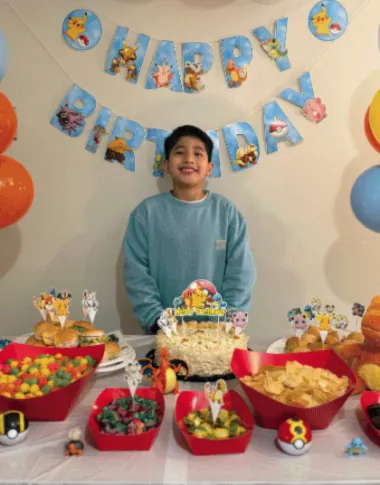 Mateo sonríe frente a su mesa de cumpleaños decorada con globos y dulces.