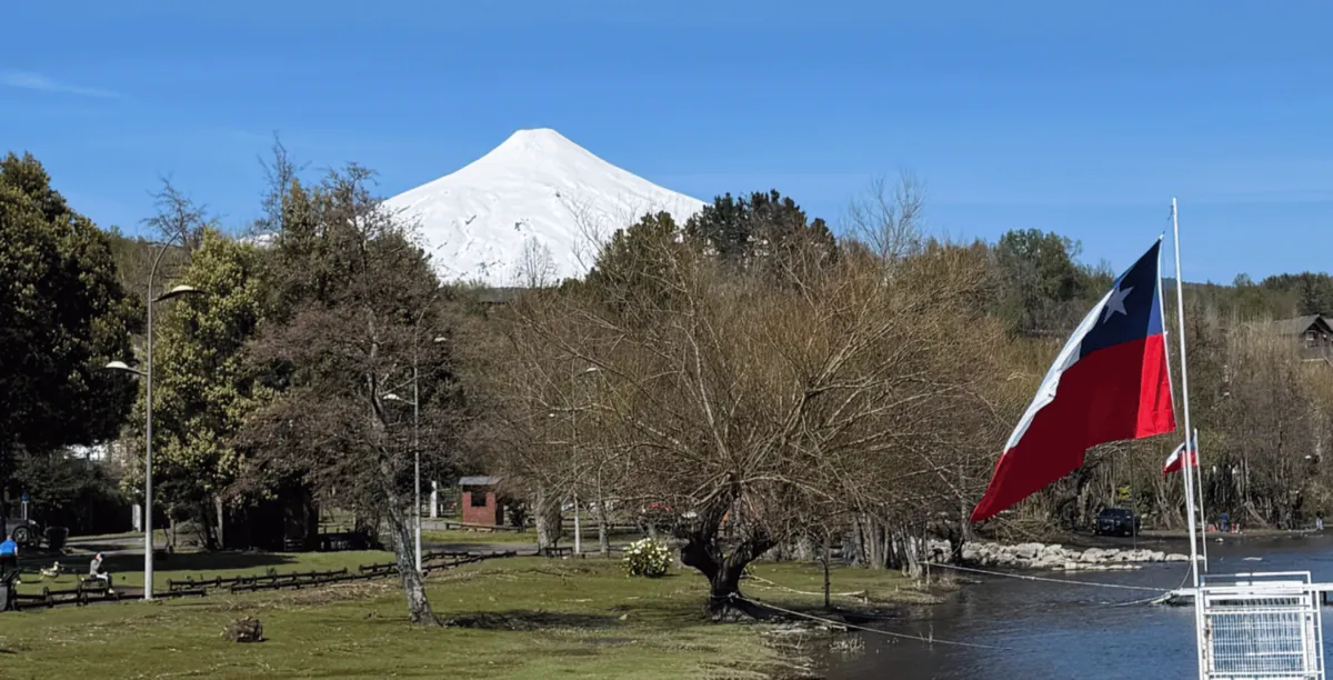 El volcán Villarrica nevado sobre Pucón, en el sur de Chile, con una bandera chilena junto al lago.